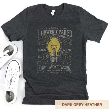 A dark grey heather Bella Canvas t-shirt featuring a lightbulb in a distressed, vintage style along with the words I haven't failed I've just found 10,000 ways that wont work Thomas A. Edison.