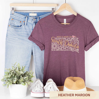 A hanging heather maroon Bella Canvas t-shirt featuring a mandala in the shape of South Dakota with the words home is where the heart is.