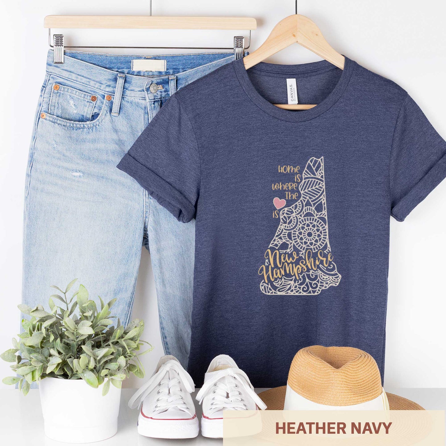 A hanging heather navy Bella Canvas t-shirt featuring a mandala in the shape of New Hampshire with the words home is where the heart is.