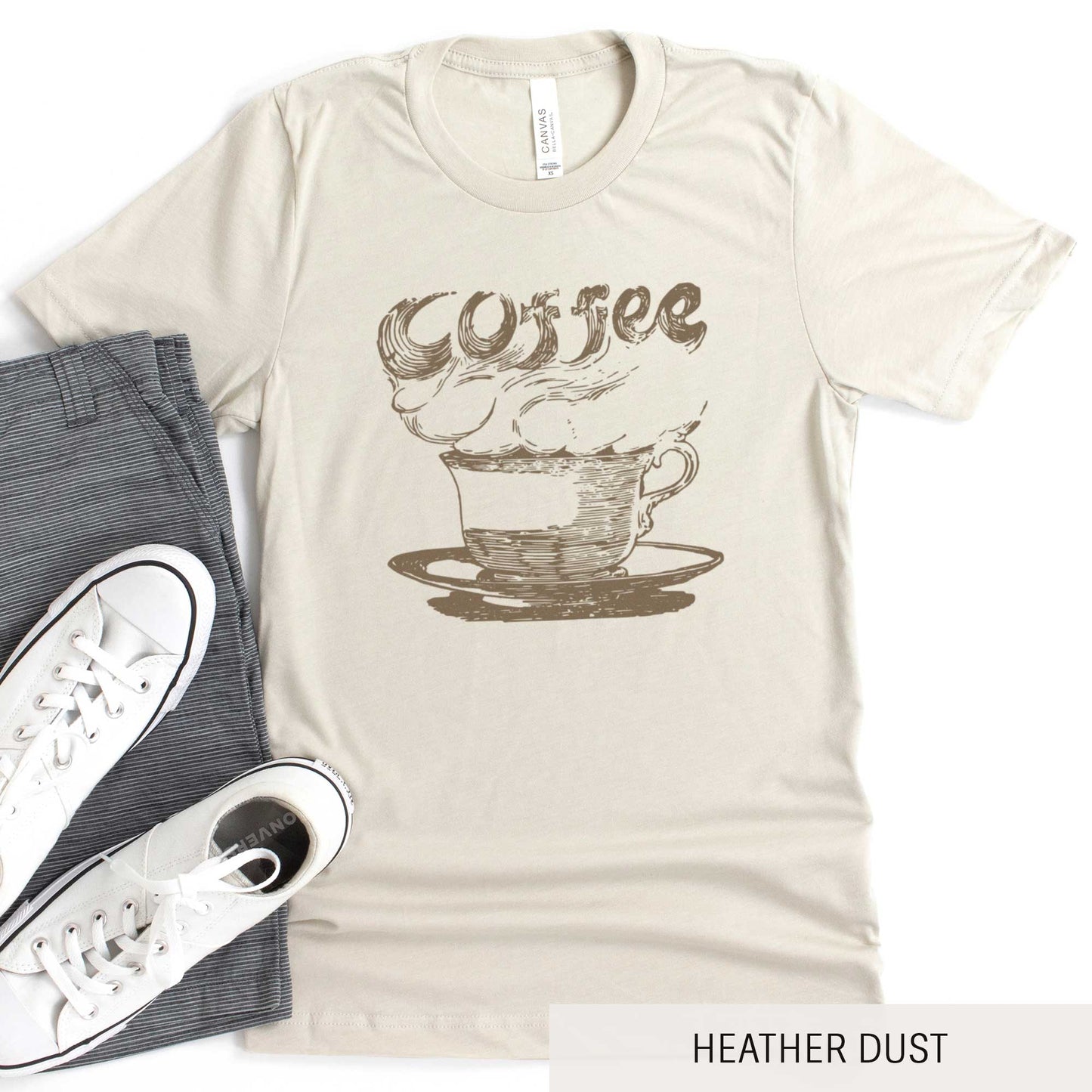 A heather dust Bella Canvas t-shirt featuring a vintage illustration of a steaming cup of coffee with the words coffee rising out from it.