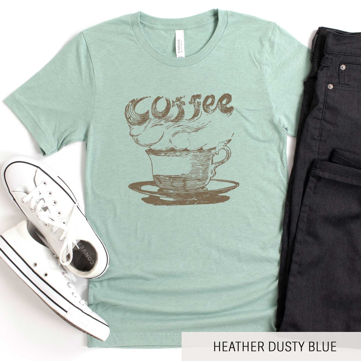 A heather dusty blue Bella Canvas t-shirt featuring a vintage illustration of a steaming cup of coffee with the words coffee rising out from it.