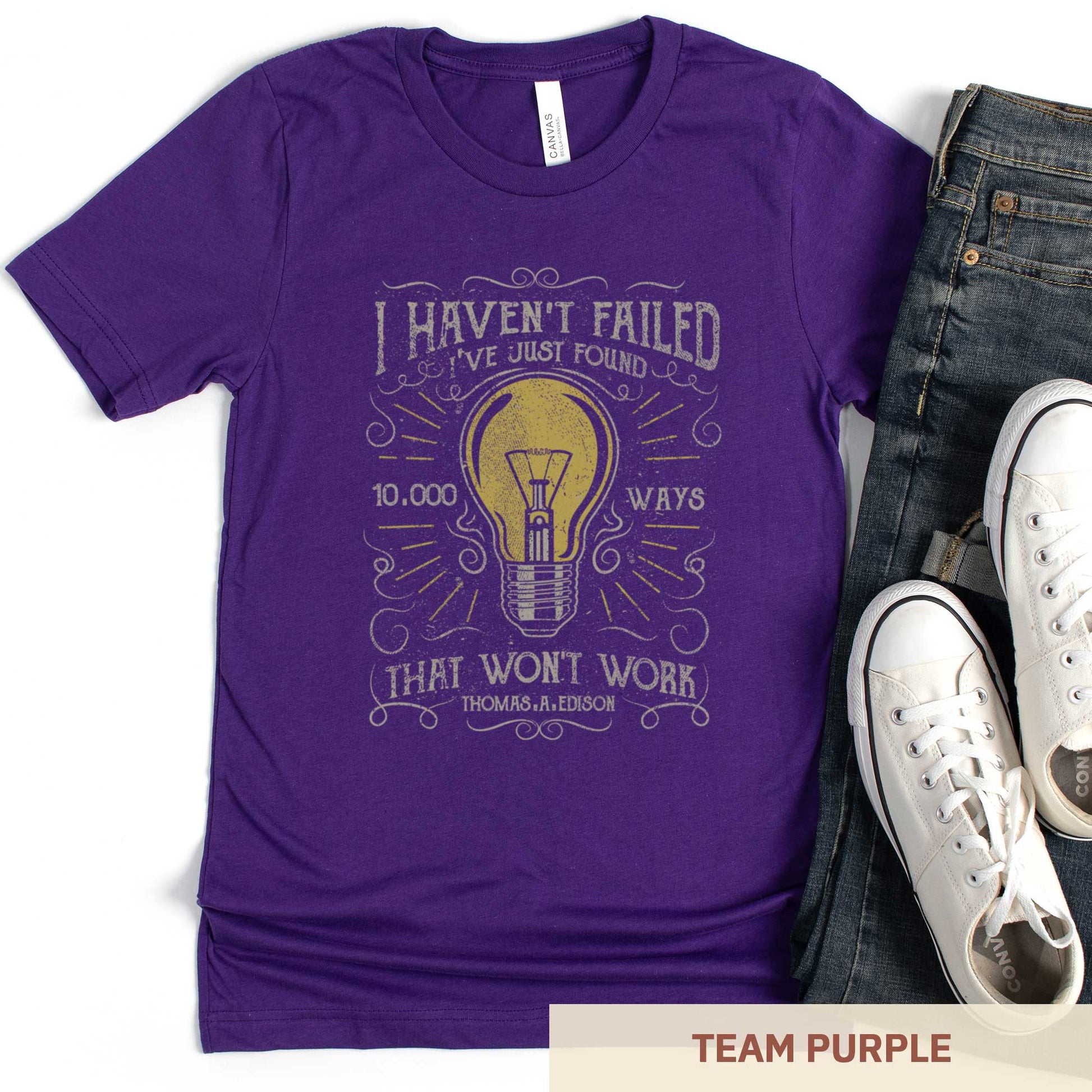 A team purple Bella Canvas t-shirt featuring a lightbulb in a distressed, vintage style along with the words I haven't failed I've just found 10,000 ways that wont work Thomas A. Edison.