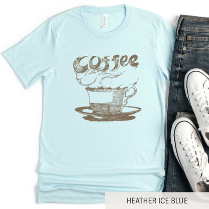 A heather ice blue Bella Canvas t-shirt featuring a vintage illustration of a steaming cup of coffee with the words coffee rising out from it.