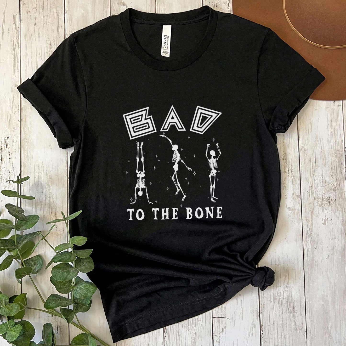 A black Bella Canvas t-shirt that says bad to the bone surrounded by skeletons.