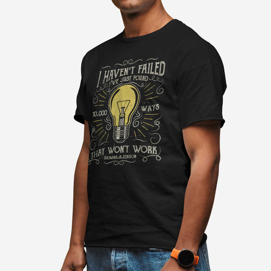 A man wearing a black Bella Canvas t-shirt featuring a lightbulb in a distressed, vintage style along with the words I haven't failed I've just found 10,000 ways that wont work Thomas A. Edison.