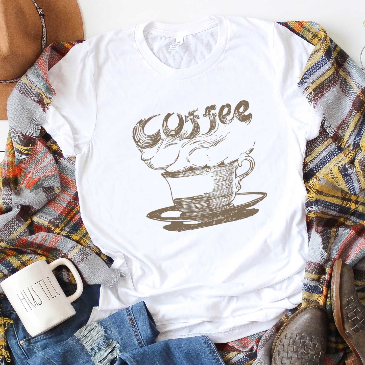 A white Bella Canvas t-shirt featuring a vintage illustration of a steaming cup of coffee with the words coffee rising out from it.