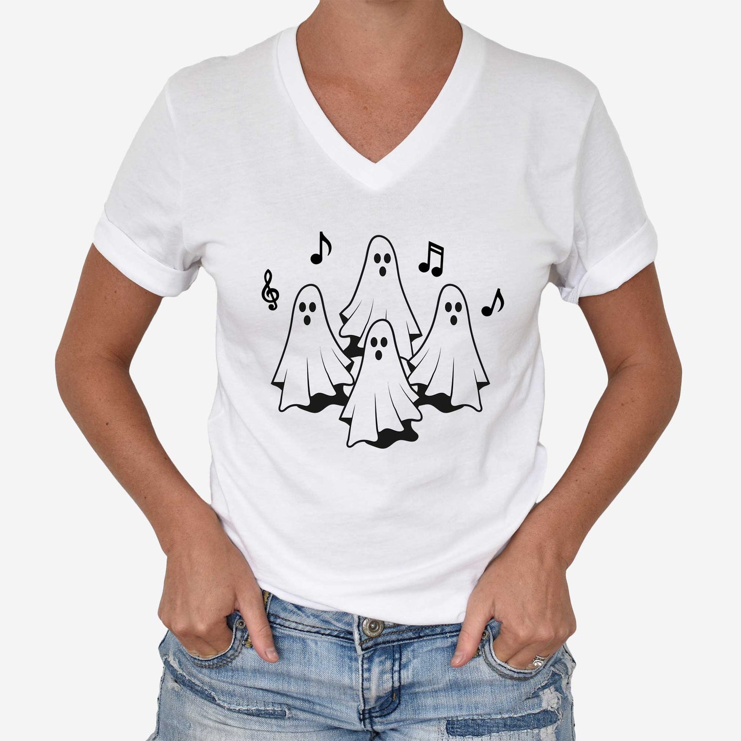 A woman wearing a white Bella Canvas v-neck t-shirt featuring four ghosts singing with musical notes.