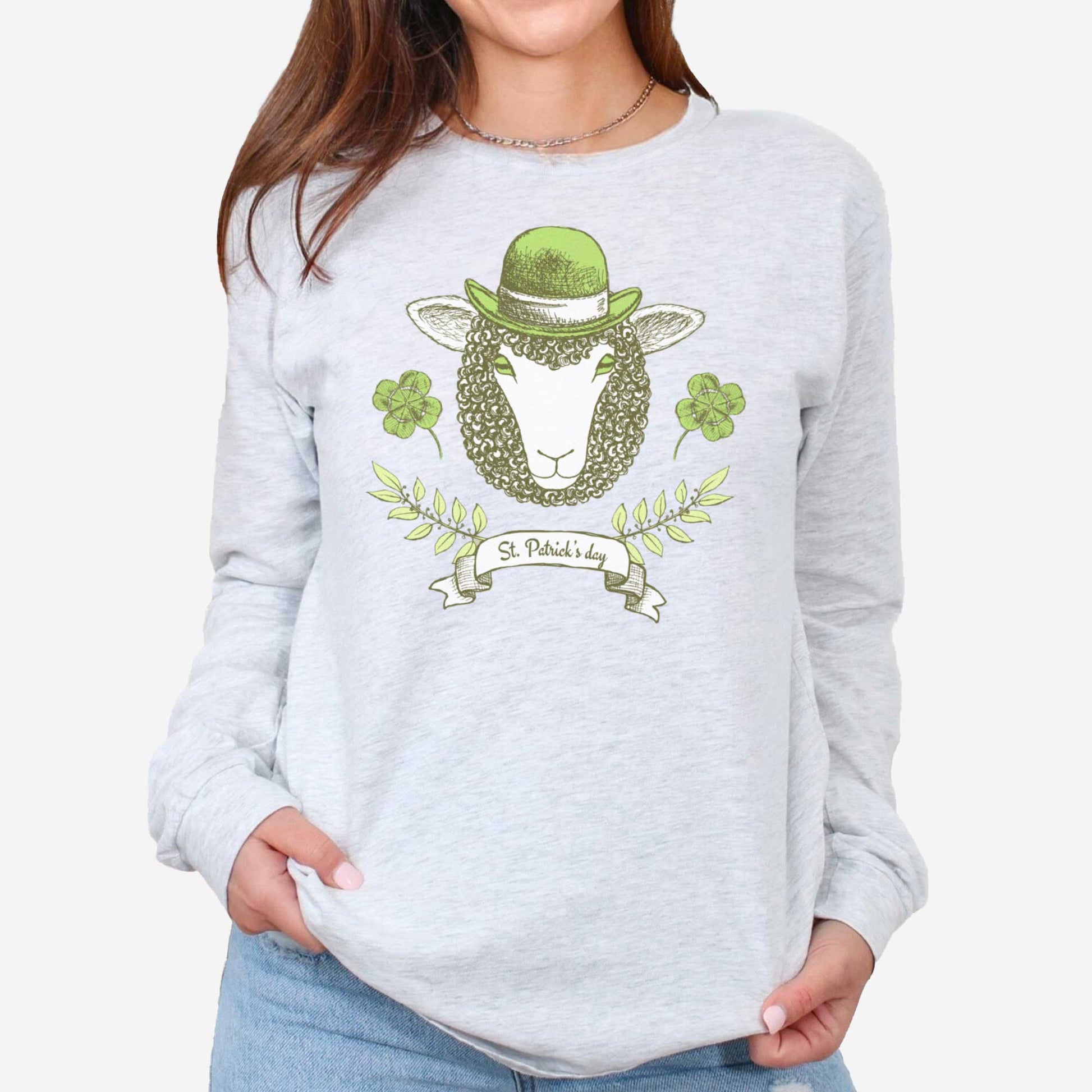 A woman wearing a long sleeved ash Bella Canvas t-shirt featuring a sheep with a green hat, clovers and the words St.Patrick's Day.