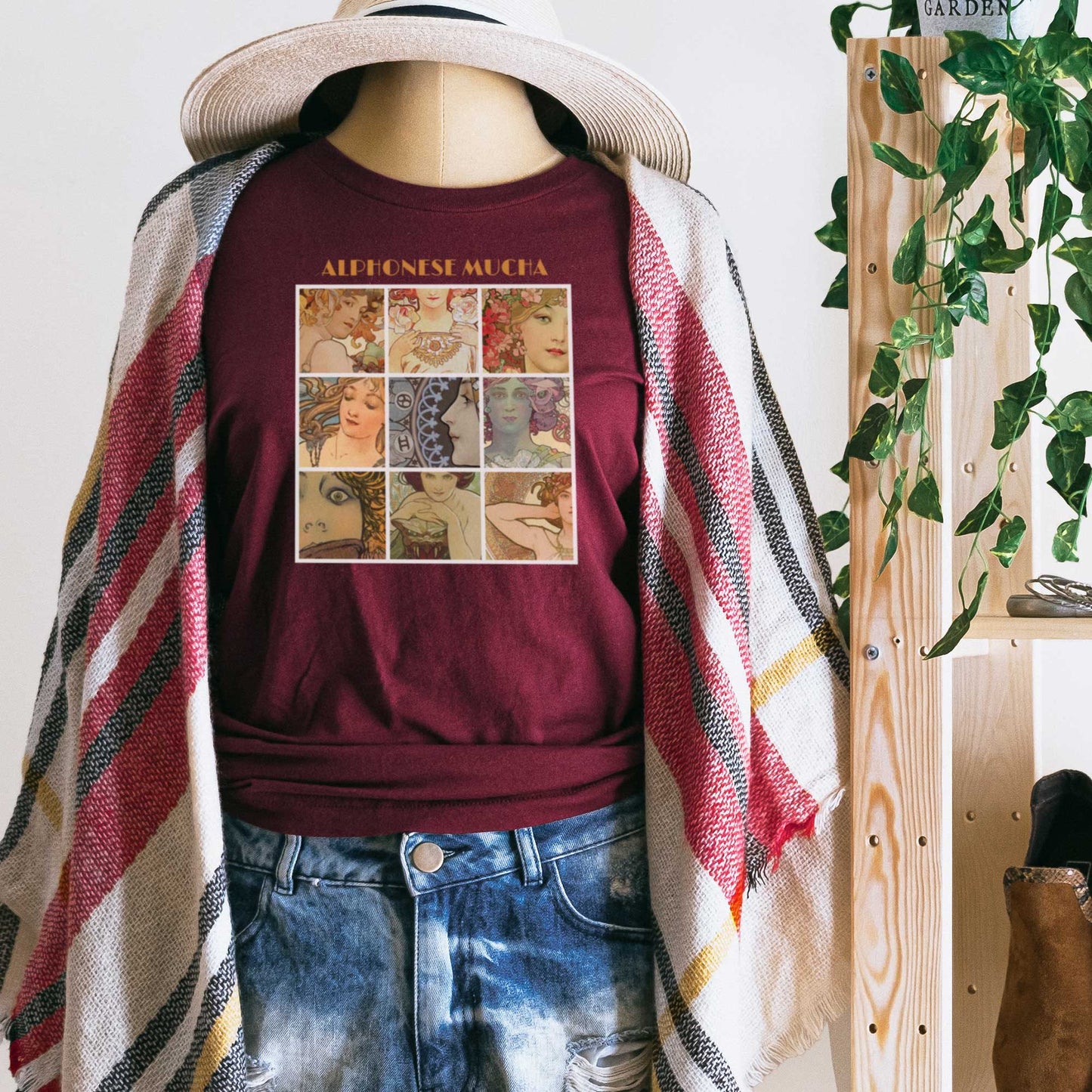 A mannequin wearing a maroon Bella Canvas t-shirt featuring a collage of female faces from Alphonse Mucha's art nouveau artwork.