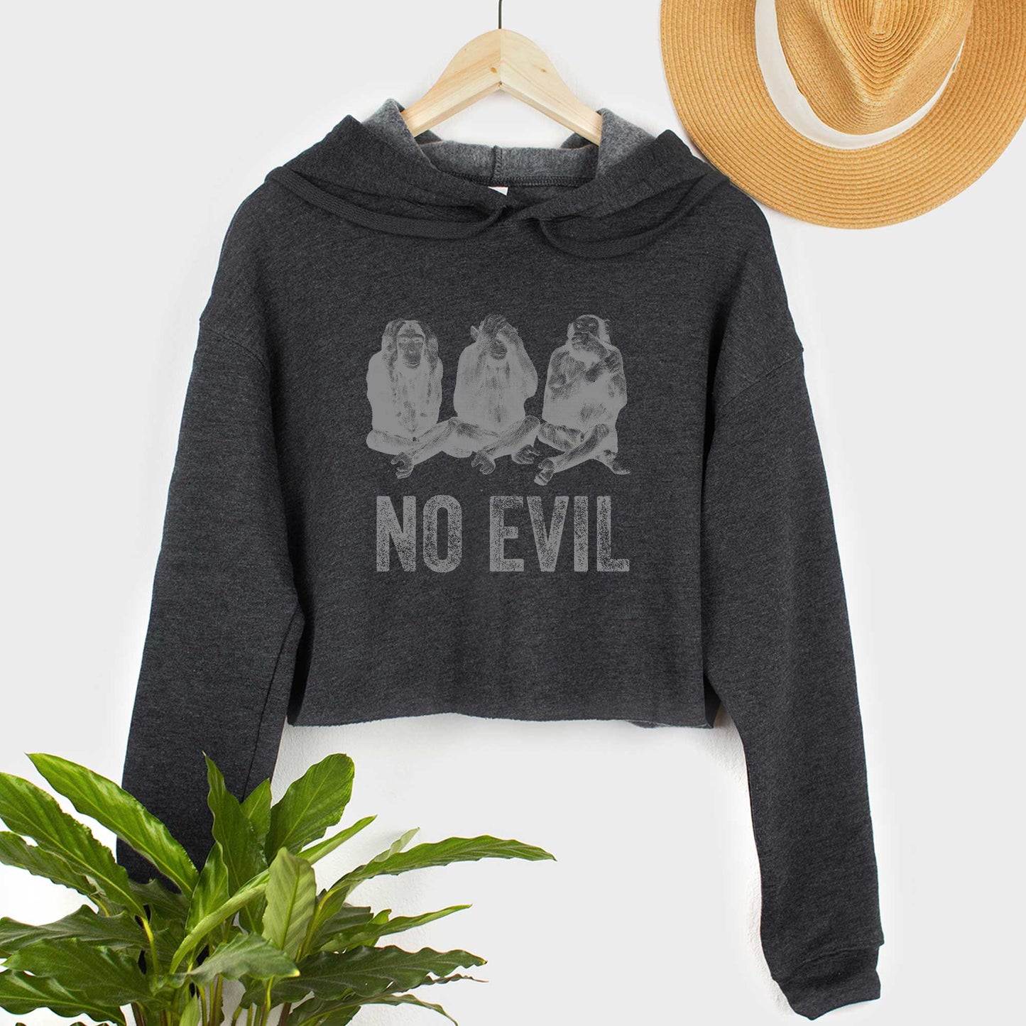 A hanging dark grey heather Bella Canvas cropped hoodie featuring 3 wise monkeys and the words no evil.