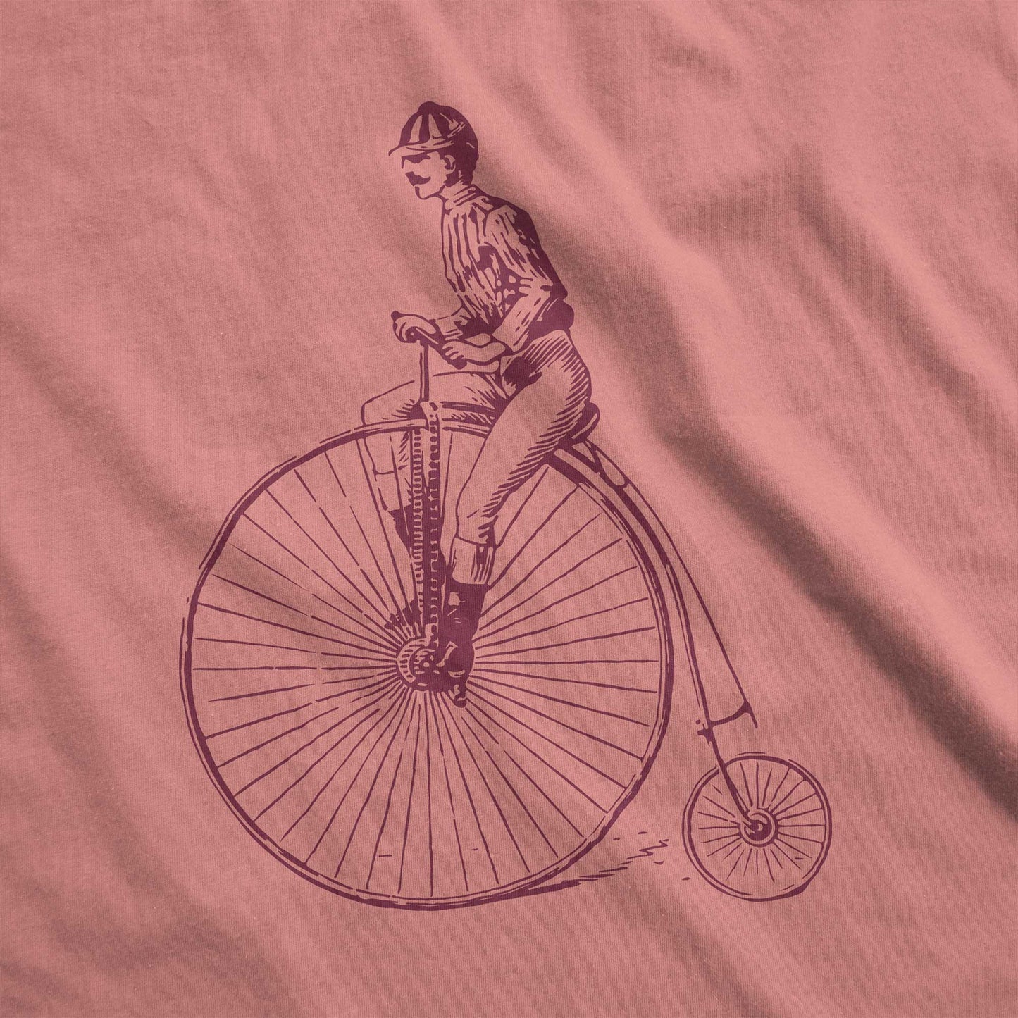 A heather mauve Bella Canvas swatch featuring a Victorian man riding a penny farthing bicycle.