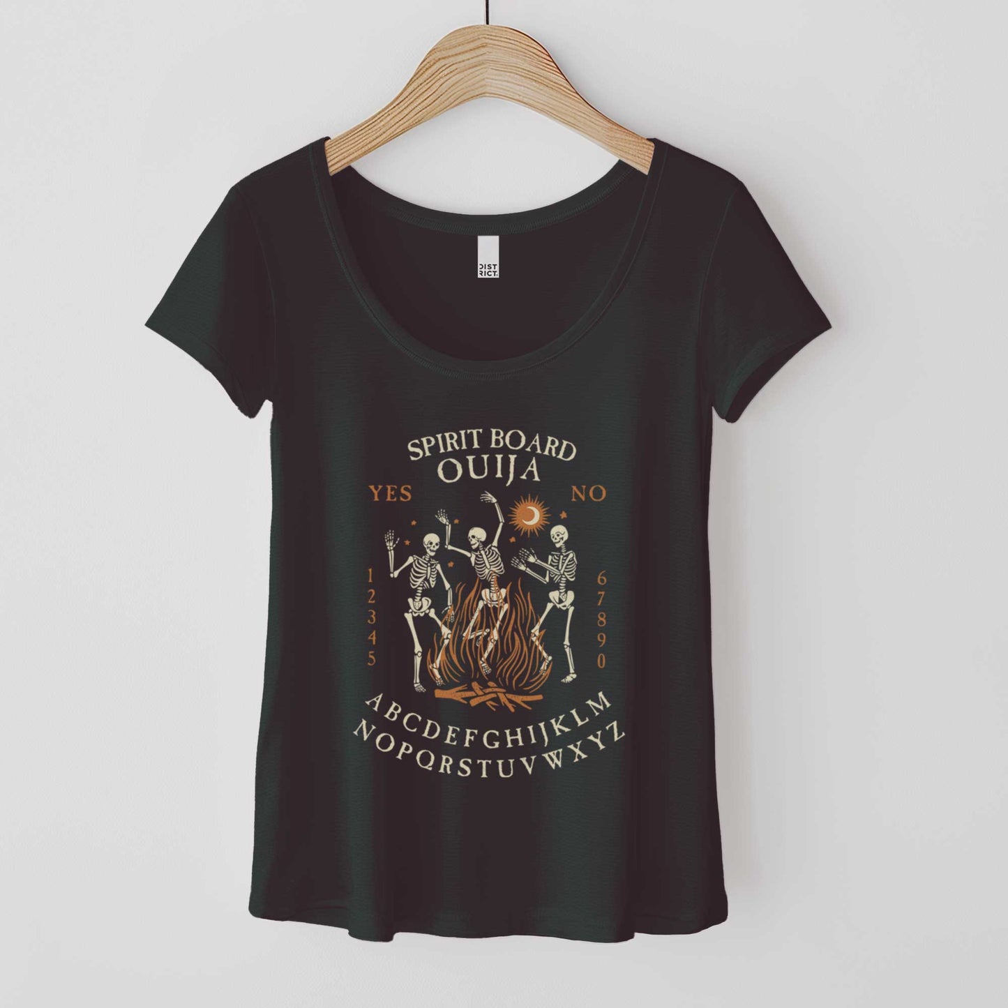 A hanging black District 7501 scoop neck t-shirt featuring dancing skeletons in front of a fire and an ouija board layout.