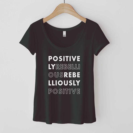 A hanging black District 7501 scoop neck t-shirt featuring the words positively rebellious rebelliously positive.