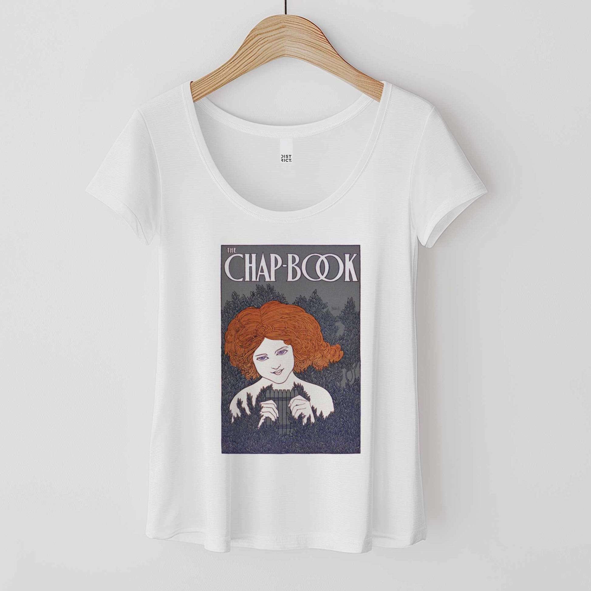 A hanging white District 7501 scoop neck t-shirt featuring a vintage cover of The Chap-Book with an illustration of a young woman in the bushes with a pan flute.