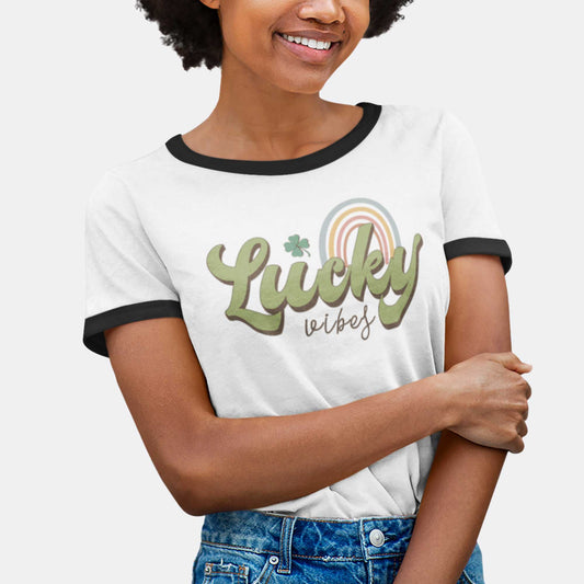 A woman wearing a white classic ringer t-shirt with black banding featuring the words lucky vibes and a rainbow.